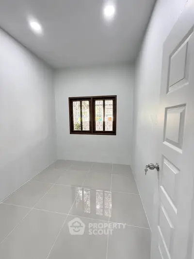 Minimalist small room with white walls and tiled floor, featuring a window with a view.