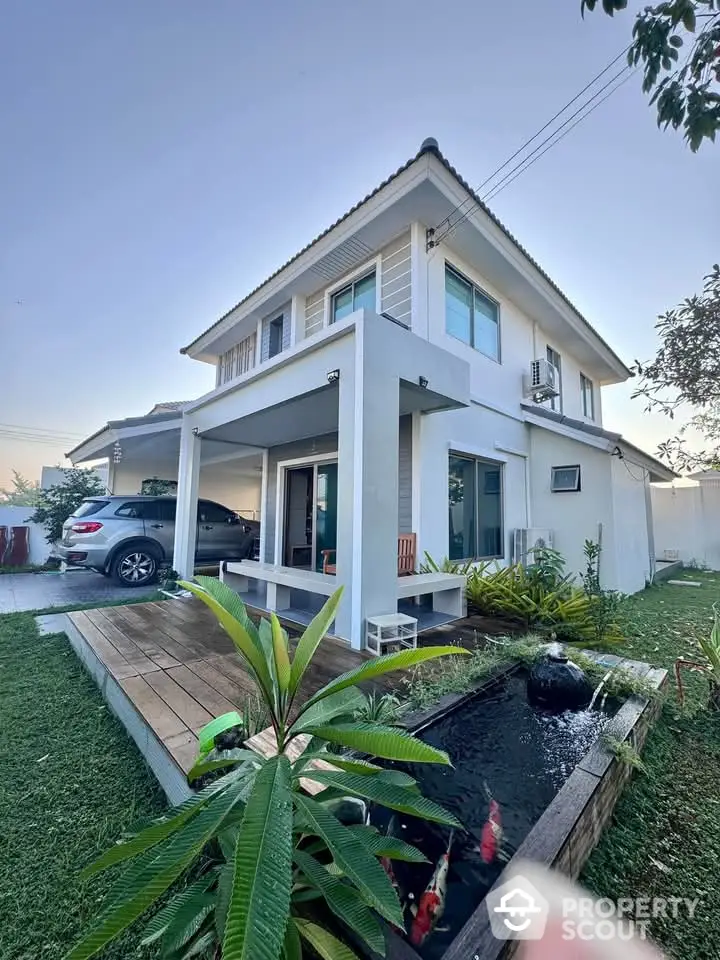 Modern two-story house with carport and garden pond, perfect for family living.