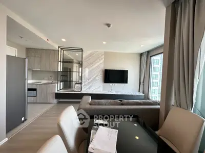 Modern living room with open kitchen, sleek furniture, and large windows offering natural light.