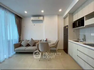 Modern open-layout living room with kitchen, featuring sleek furniture and natural light.