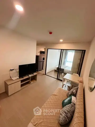 Modern living room with cozy sofa, TV, and dining area in open-plan apartment.
