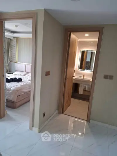 Modern apartment hallway with view into bedroom and bathroom, featuring elegant decor and lighting.