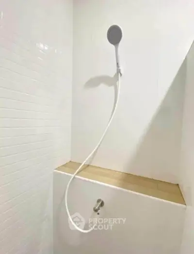 Minimalist white bathroom shower with modern handheld showerhead and tiled wall.