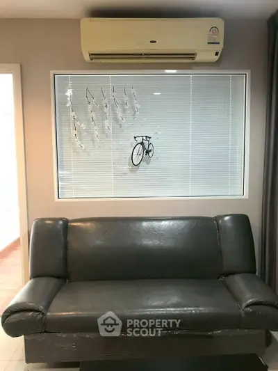 Modern living room with sleek black sofa and wall-mounted air conditioner, featuring stylish decor.