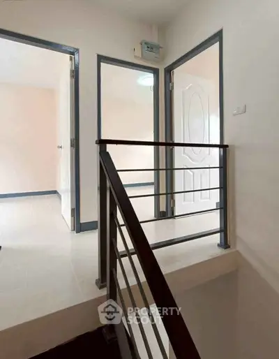 Modern interior hallway with sleek railing and open doors leading to bright rooms.