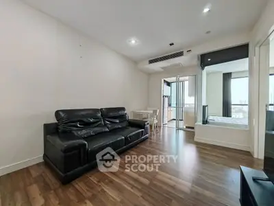 Spacious modern living room with sleek black leather sofa and wooden flooring, featuring a view of the city skyline.