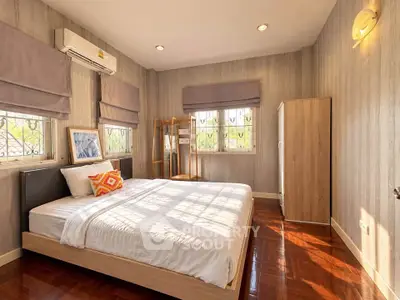 Spacious bedroom with wooden flooring and natural light, featuring modern decor and air conditioning.