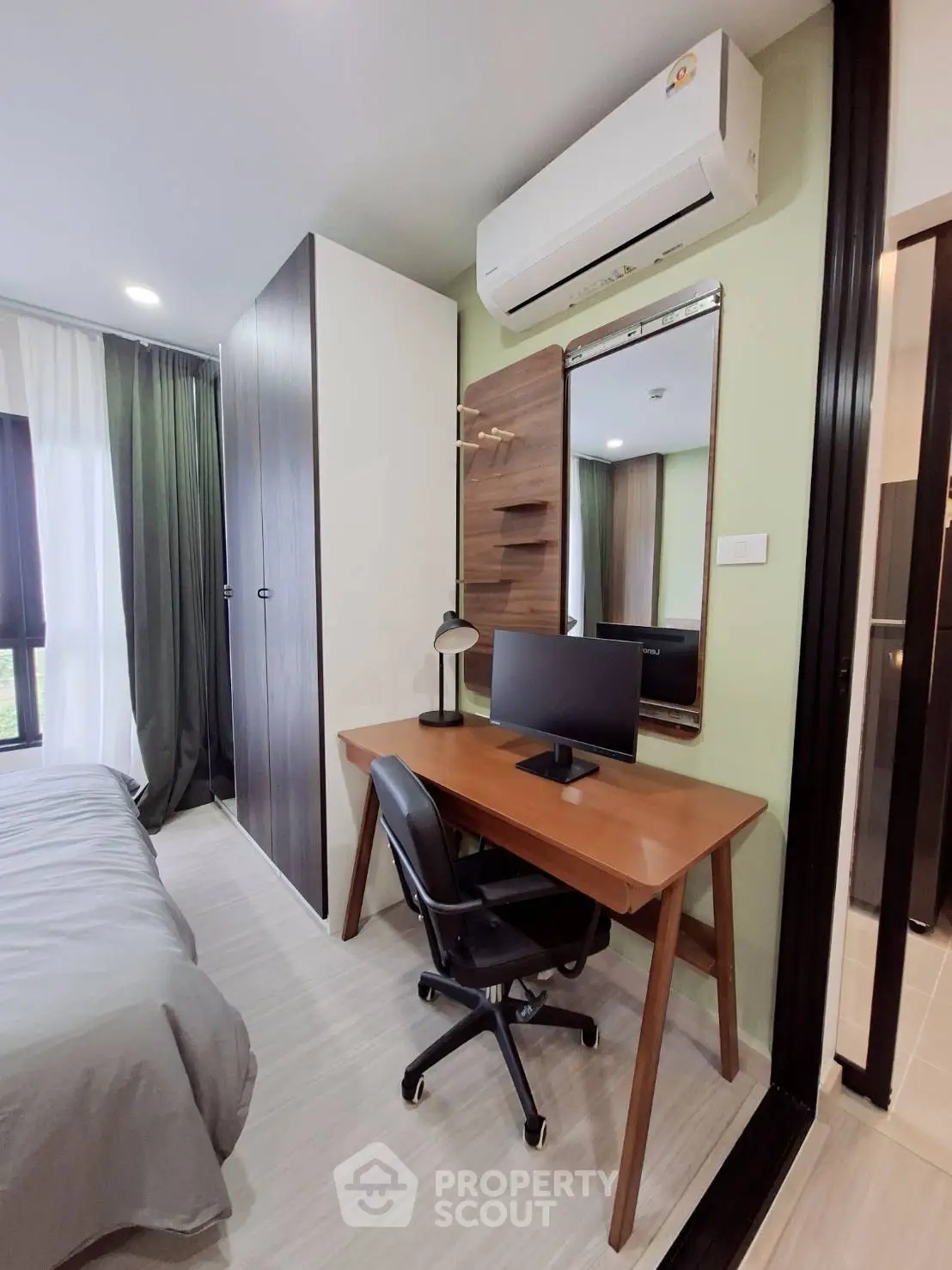 Modern bedroom with study area, featuring sleek desk, chair, and wall-mounted mirror under air conditioning unit.