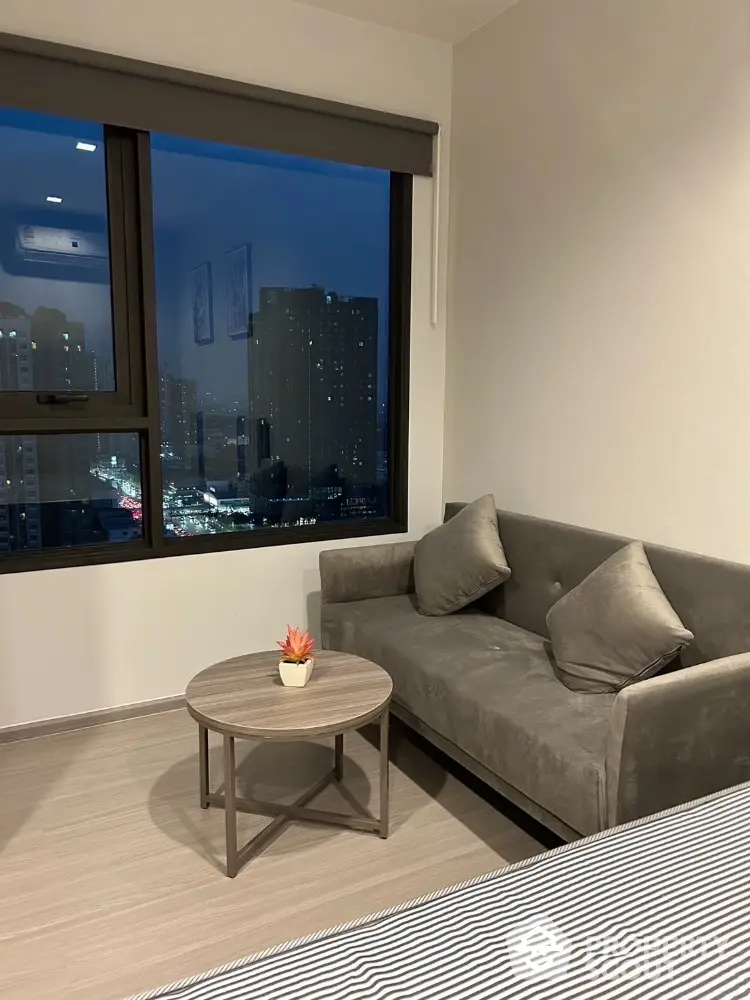 Cozy bedroom with city view, featuring a stylish gray sofa and modern decor.