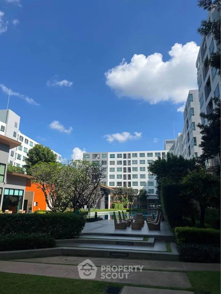 Stunning modern apartment complex with lush garden and outdoor seating under a clear blue sky.