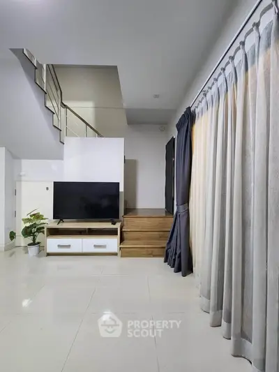 Spacious modern living room with sleek staircase and large TV, perfect for contemporary living.
