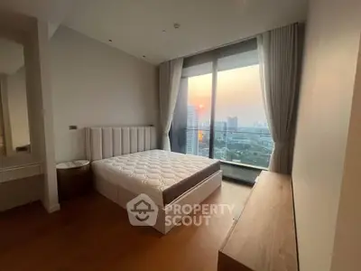 Spacious bedroom with large window offering stunning city view at sunset.