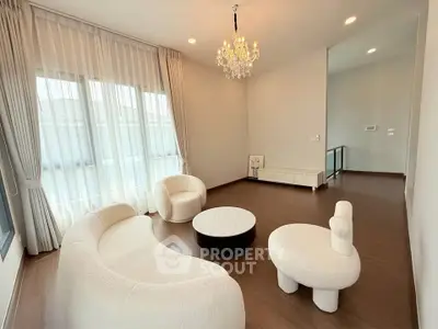 Elegant living room with modern white furniture and chandelier, featuring large windows and wooden flooring.