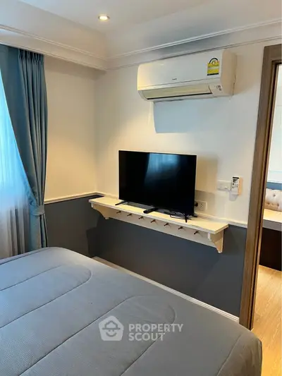 Modern bedroom with air conditioning and wall-mounted TV, featuring elegant blue curtains and cozy bedding.