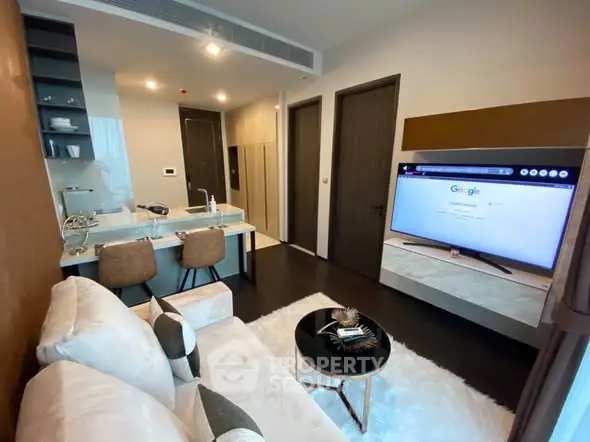 Modern living room with open kitchen, stylish decor, and large TV in a cozy apartment setting.