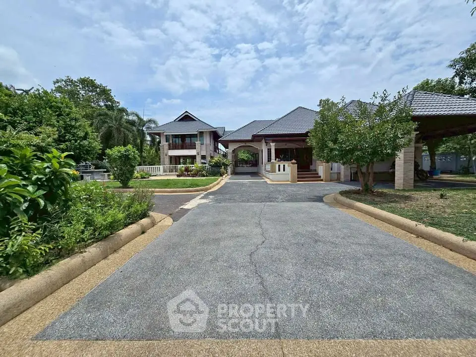 Spacious driveway leading to a luxurious villa with lush greenery and modern architecture.