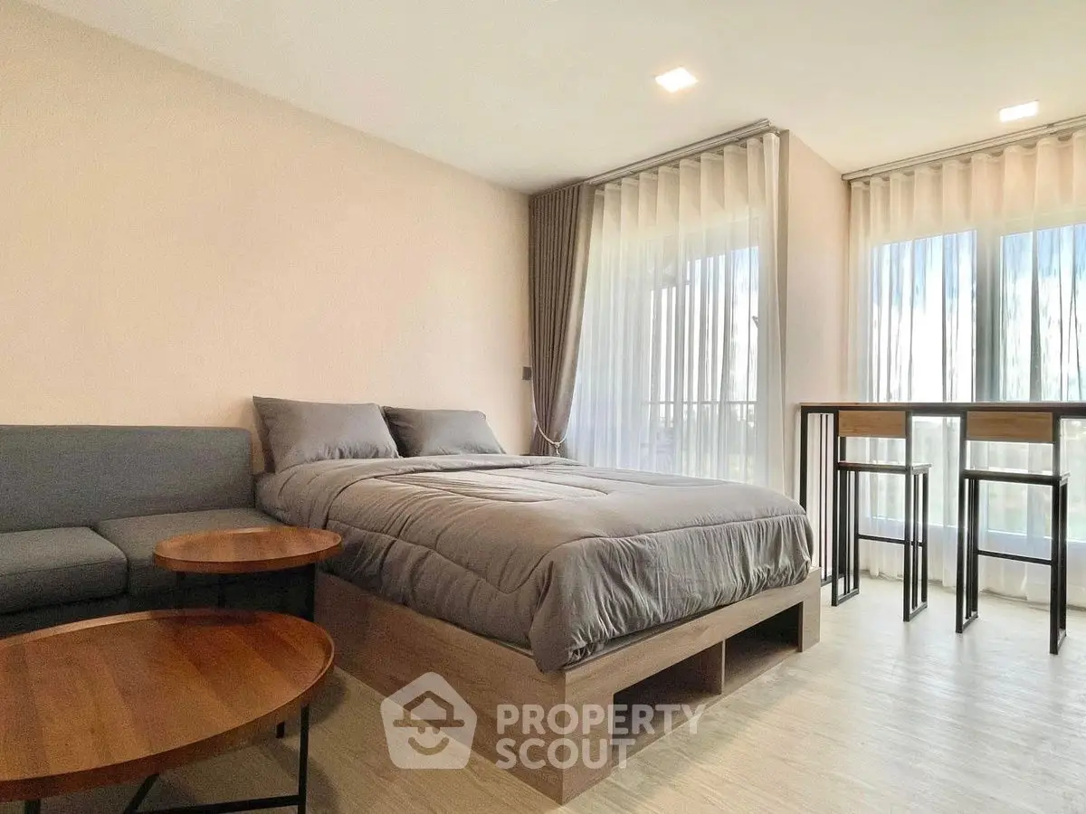 Modern bedroom with cozy bed, stylish sofa, and natural light from large windows.