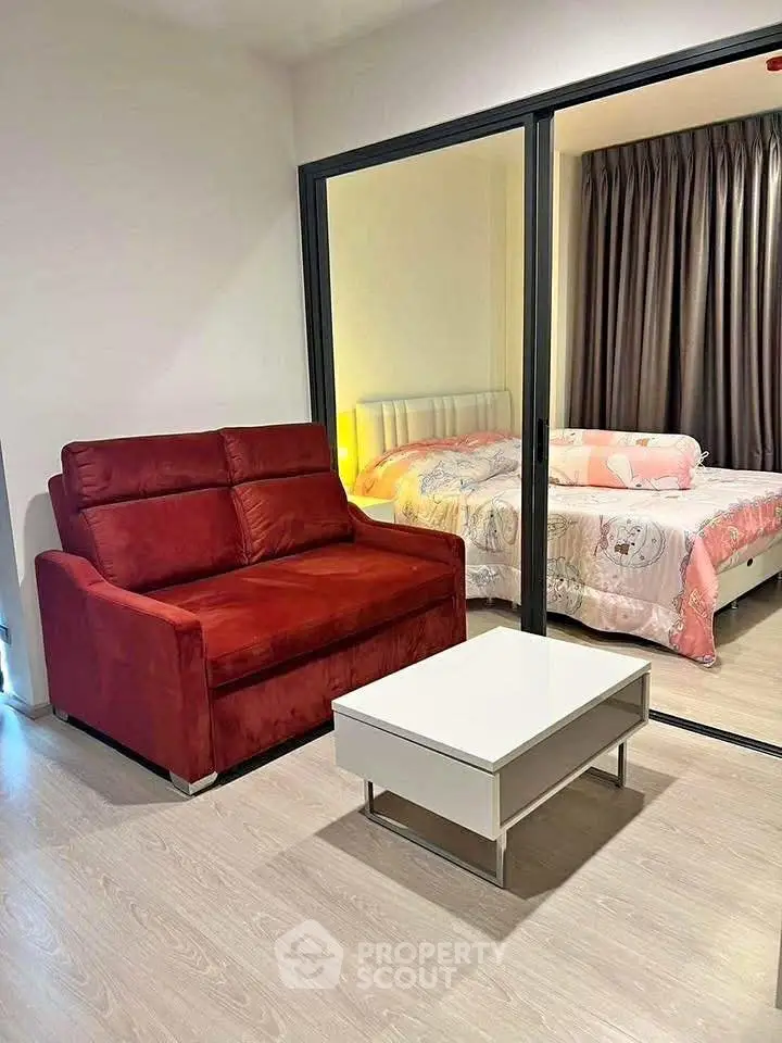 Modern apartment with cozy living room and stylish bedroom separated by glass wall, featuring elegant furnishings.