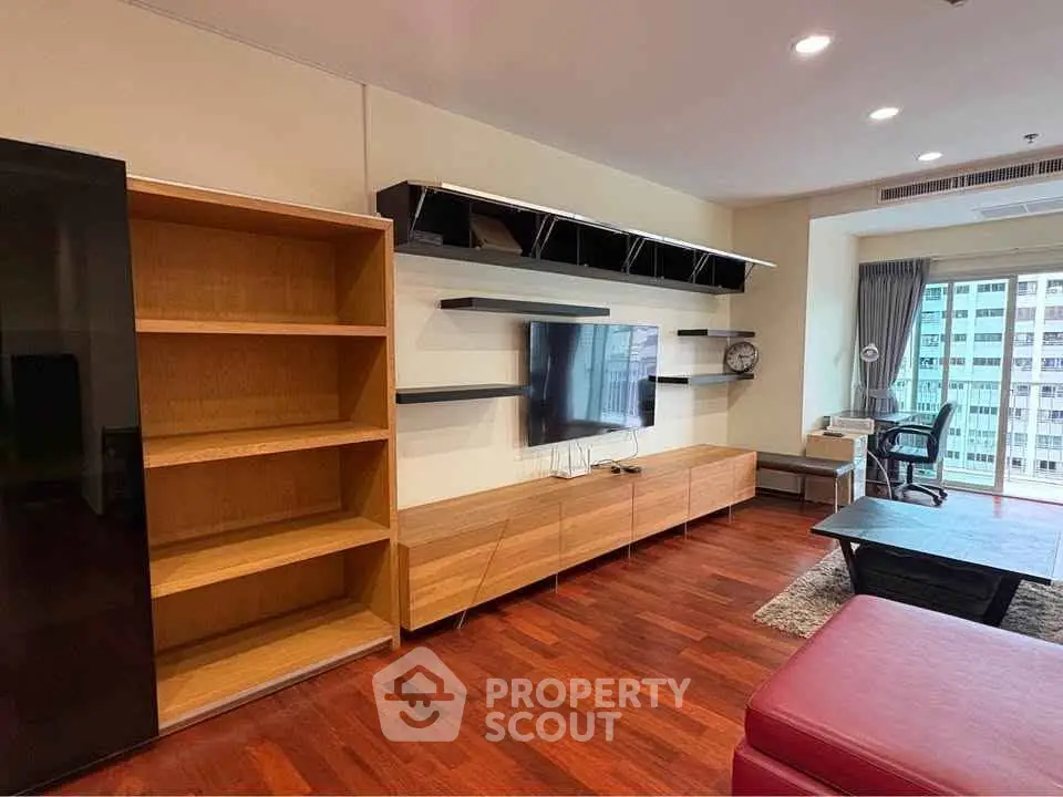 Spacious living room with modern TV setup and wooden flooring in high-rise apartment.