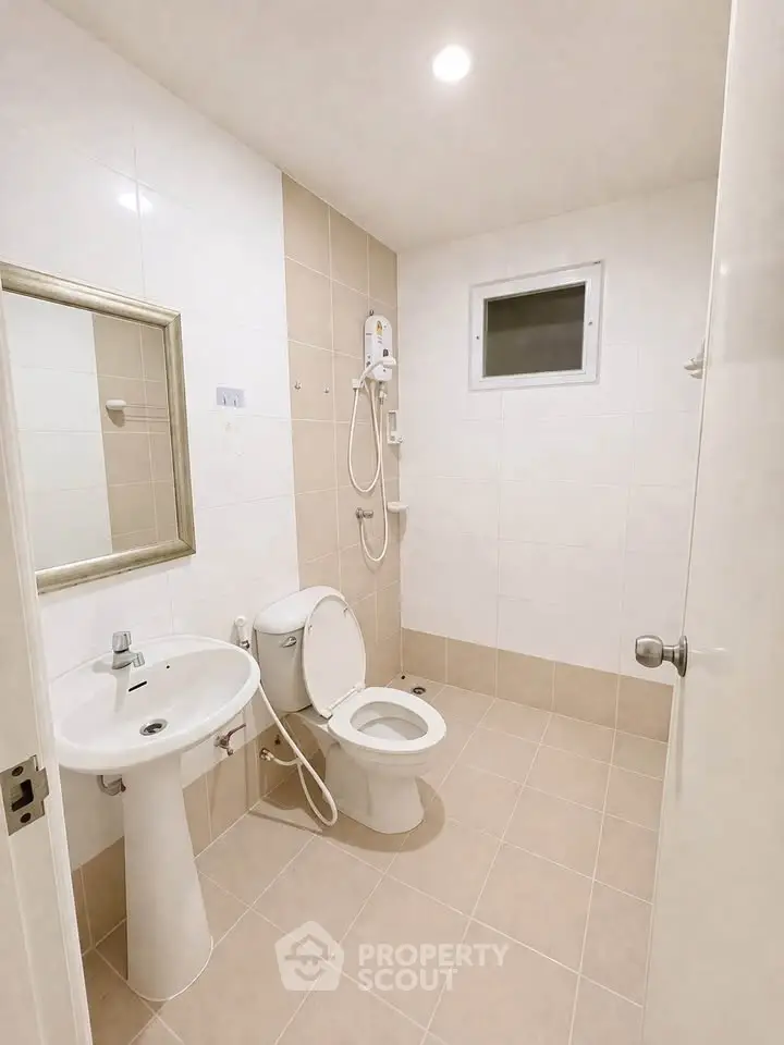 Modern bathroom with sleek fixtures and neutral tiles, featuring a shower and pedestal sink.