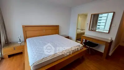Spacious bedroom with modern wooden furniture and ensuite bathroom in a high-rise apartment.