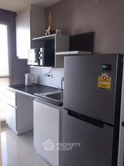 Modern kitchen with sleek cabinets, stainless steel fridge, and microwave in a compact layout.