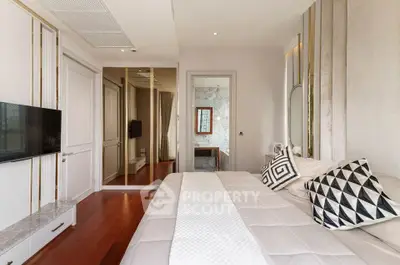 Elegantly designed bedroom with polished wooden floors, luxurious white bedding, and modern geometric accent pillows, complemented by sleek gold and white wall panels.