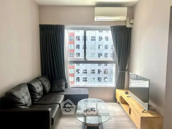 Modern living room with large window and city view, featuring a black leather sofa and sleek TV setup.