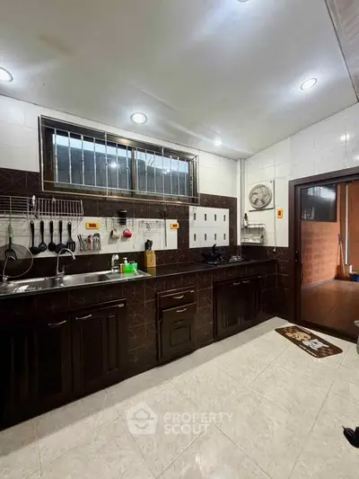 Spacious kitchen with modern dark wood cabinets and stainless steel sink, featuring open layout and ample lighting.