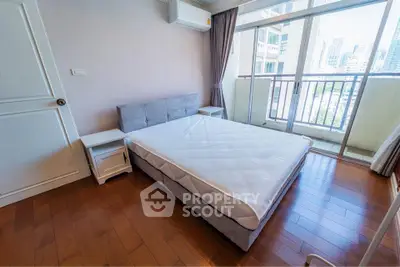 Spacious bedroom with balcony and city view, featuring hardwood floors and modern furnishings.