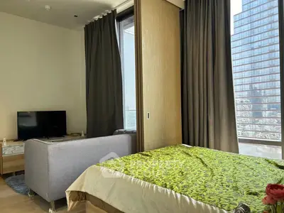 Modern bedroom with city view, featuring a cozy bed, sleek TV setup, and floor-to-ceiling windows.
