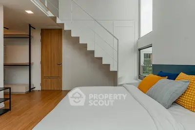 Modern bedroom with loft-style staircase and large windows for natural light.