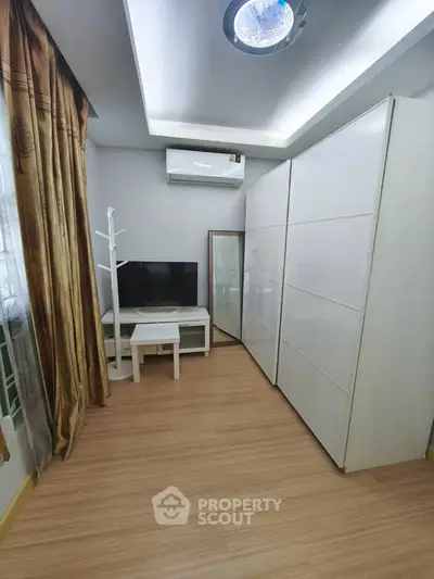 Modern bedroom with sleek wardrobe and wall-mounted TV, featuring elegant curtains and wooden flooring.