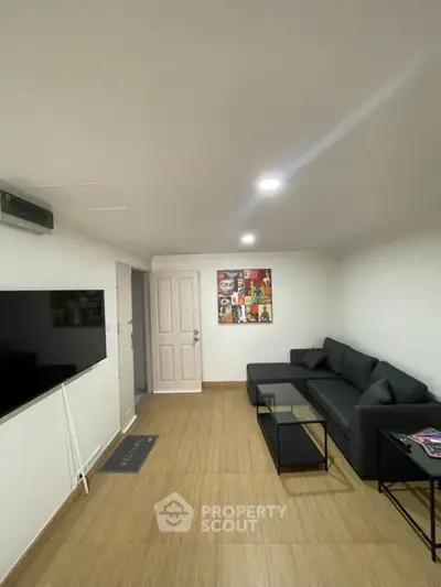 Modern living room with sleek black sofa and wall-mounted TV, perfect for relaxation.