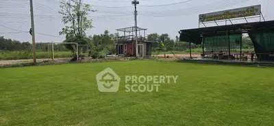 Expansive green field with rustic outdoor seating area and small building, ideal for recreational activities.