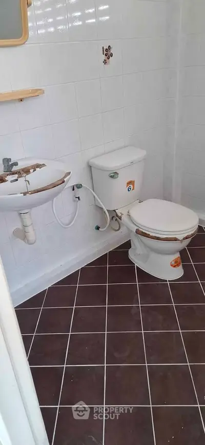 Compact bathroom with white tiles and brown floor, featuring a sink and toilet.