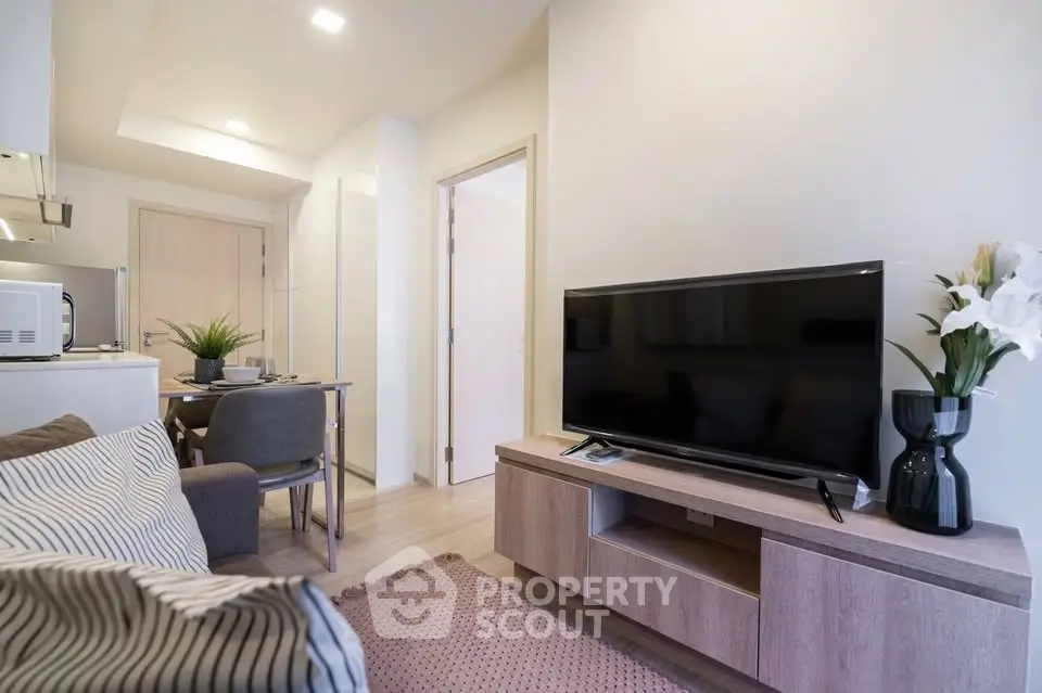 Modern living room with sleek TV setup and cozy dining area in open-plan apartment.