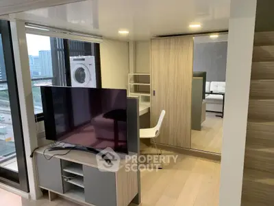 Modern studio apartment with sleek furniture and city view, featuring a wall-mounted TV and in-unit washer.