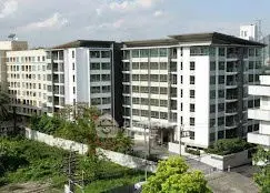 Modern multi-story residential building with lush greenery and clear sky.