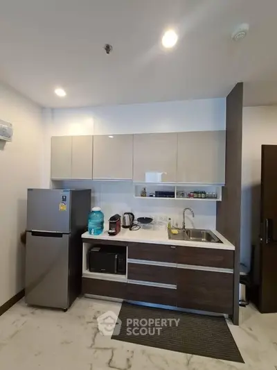 Modern kitchen with sleek cabinetry, stainless steel fridge, and microwave in a stylish apartment.