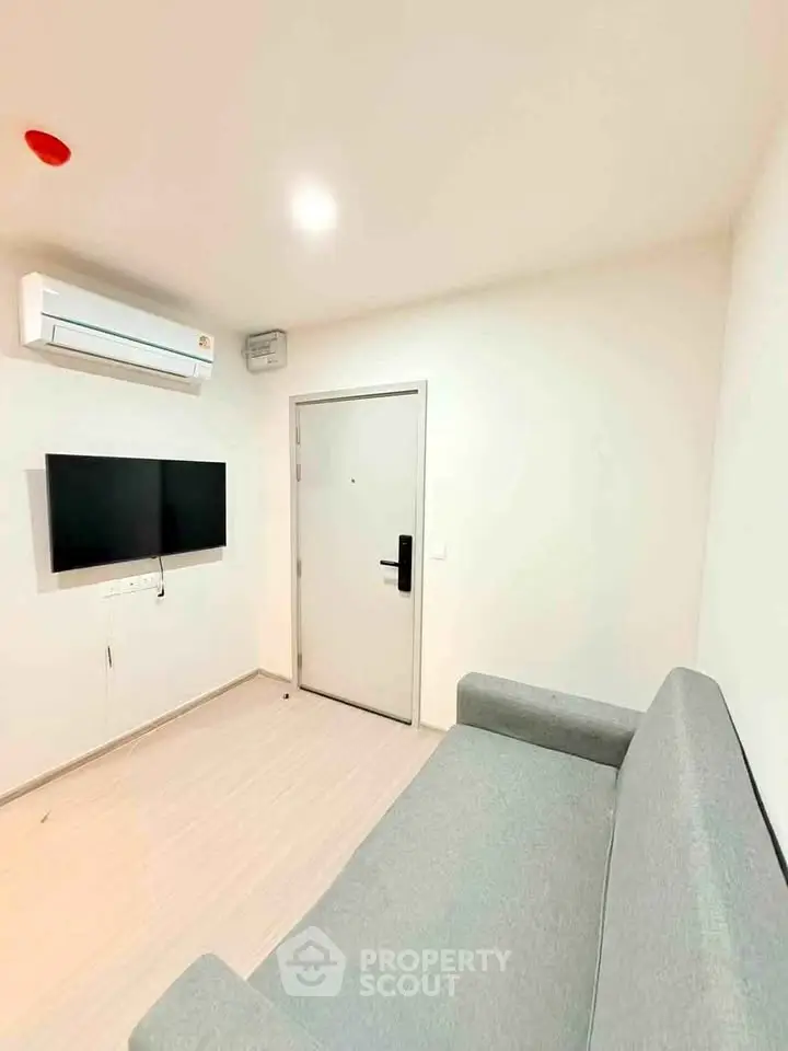 Modern living room with sleek sofa, wall-mounted TV, and air conditioning in a minimalist design.