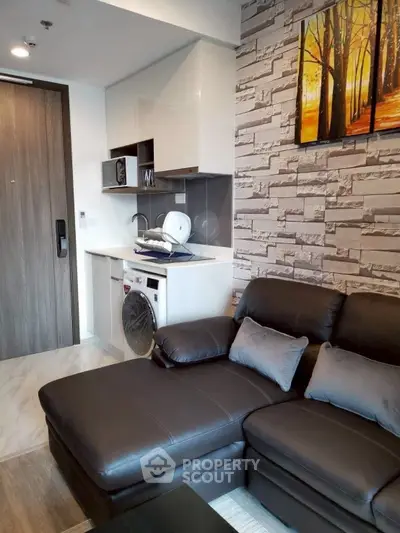 Modern living room with sleek leather sofa and compact kitchen area in stylish apartment.
