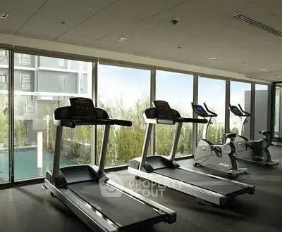Modern gym with treadmills and exercise bikes overlooking a pool view in a luxury apartment complex.