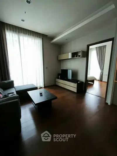 Modern living room with sleek furniture and wooden flooring, leading to a cozy bedroom.