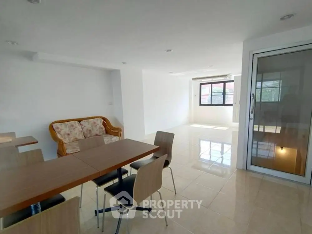 Spacious and well-lit living room with large dining table, comfortable seating, and gleaming tiled floors, leading to a sunny balcony with a view.