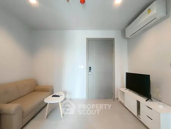 Modern living room with minimalist decor, featuring a beige sofa, flat-screen TV, and sleek air conditioning unit.