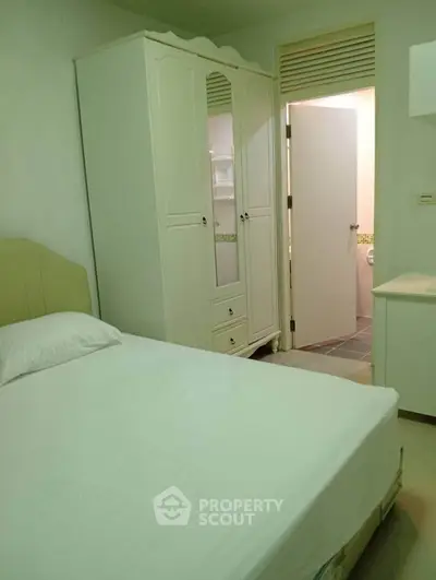 Cozy bedroom with white wardrobe and open bathroom door, ideal for compact living spaces.