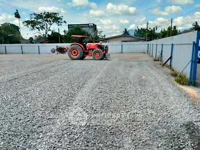 Spacious gravel lot with a tractor, ideal for development or storage, surrounded by fencing under a clear sky.