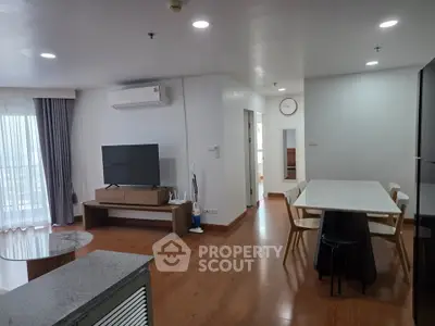 Spacious modern living room with dining area and large TV, featuring wooden flooring and natural light.