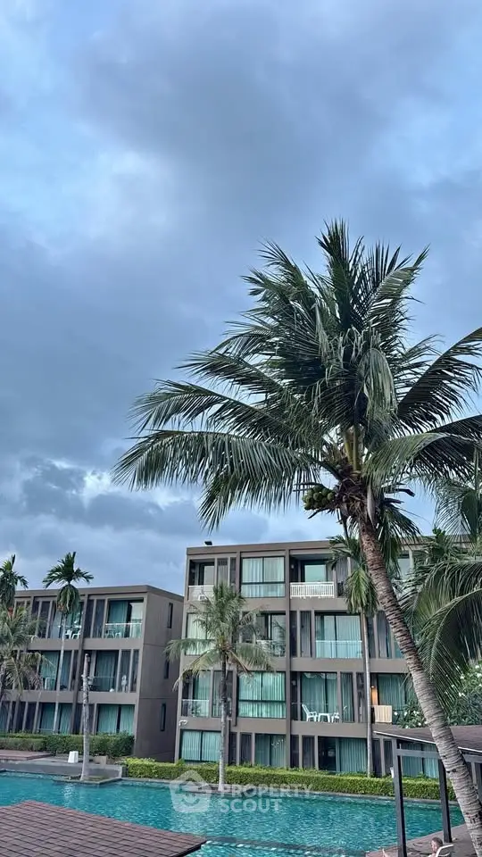 Luxurious beachfront condominium with palm trees and pool, offering serene ocean views and modern living spaces.